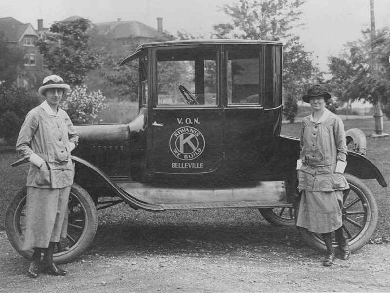 Black and white image of 2 VON nurses standing next to car in Belleville, Ontario, early 1900s